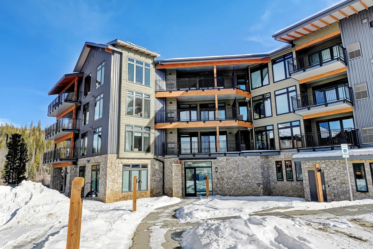 A welcoming exterior shot of a modern mountain lodge with large glass windows and a snow-covered landscape. Guests are visible skiing, snowboarding, hiking, and relaxing on balconies, creating a sense of arrival and anticipation for mountain adventures.