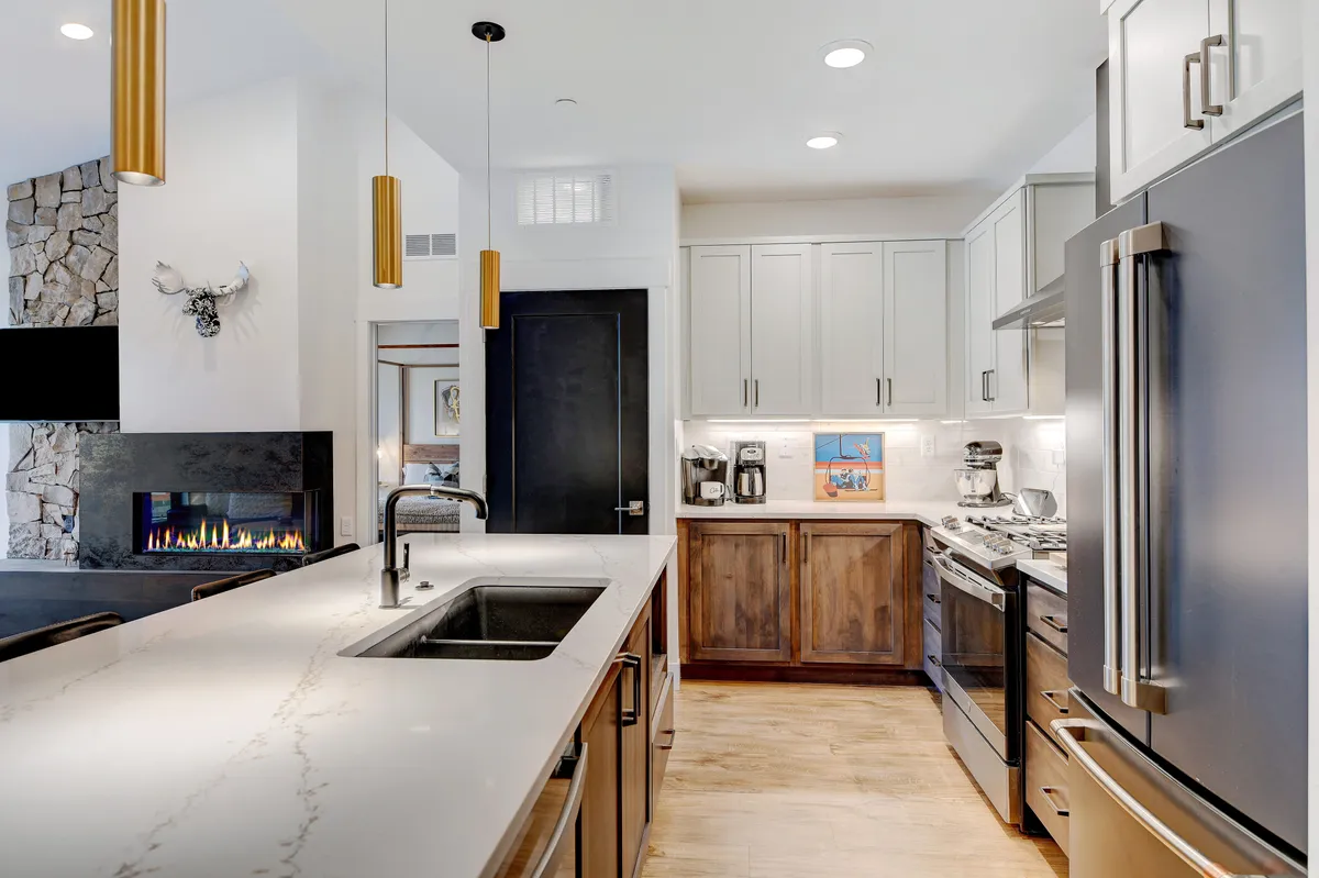 This image captures the heart of the penthouse kitchen, featuring a spacious island, a sleek sink, stainless steel appliances, and a cozy fireplace in the backdrop. The environment is warm and inviting, making it perfect for both cooking and entertaining.