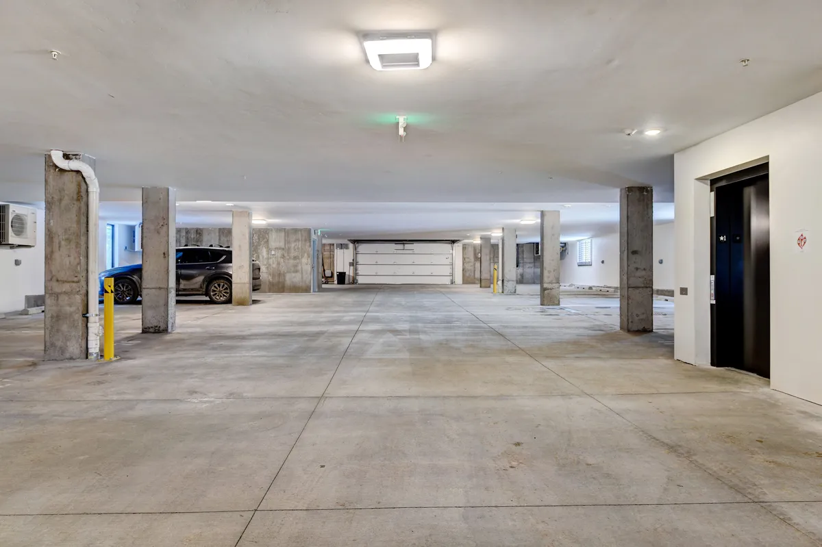 An interior view of a heated garage with concrete pillars, an elevator, and well-lit parking spaces. The scene is practical and highlights secure, convenient parking access.