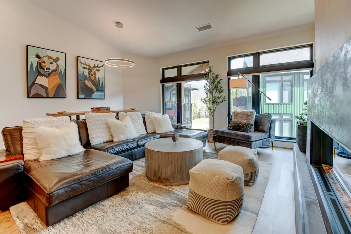 A welcoming and comfortable living room with a plush sofa, modern circular coffee table, fireplace, and artwork on the walls. Natural sunlight streams in through the windows, suggesting a bright, airy atmosphere perfect for relaxation or gathering with friends and family.