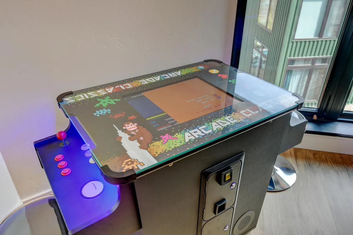 A fun and inviting arcade corner features a classic arcade machine with colorful buttons and a prominent screen. The setting suggests friendly competition and laughter, adding a playful element to the shared entertainment lounge.