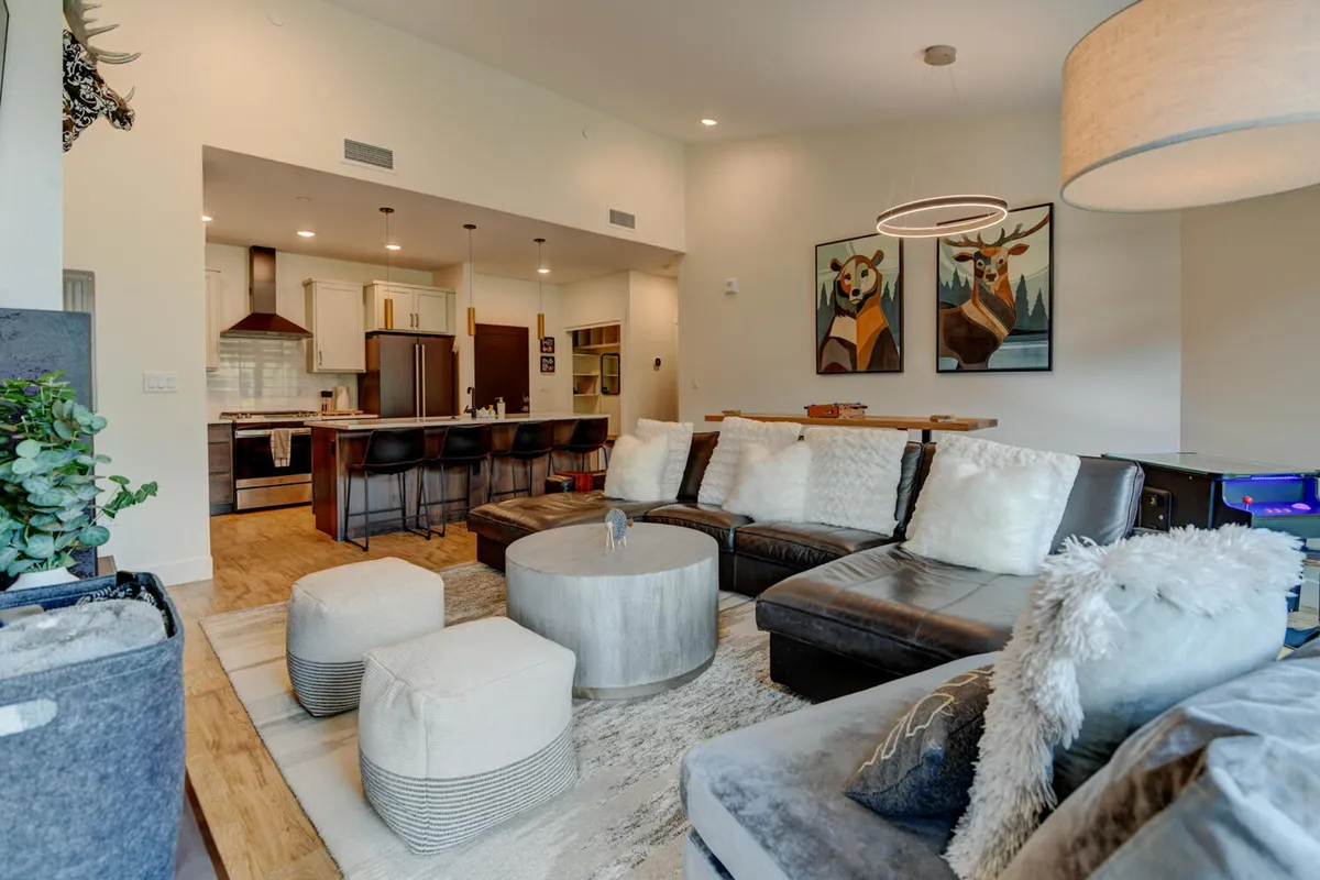A cozy living room scene with a sofa adorned with decorative pillows, a round coffee table ideal for board games, and art on the walls. The layout is perfect for intimate family gatherings, watching movies, or friendly competitions.