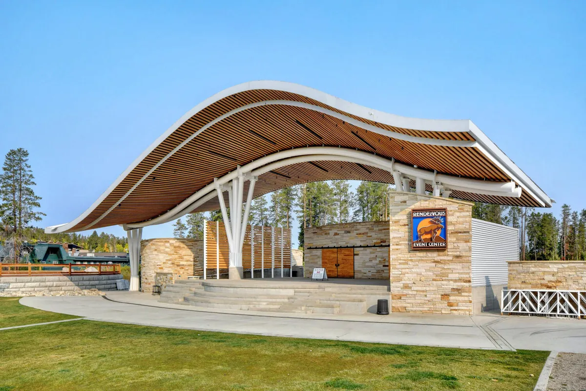 The distinctive curved roof structure and stone facade of the Hideaway Park amphitheater, with event signage visible. The area is ready for community events, concerts, and celebrations, conveying the spirit of year-round entertainment.