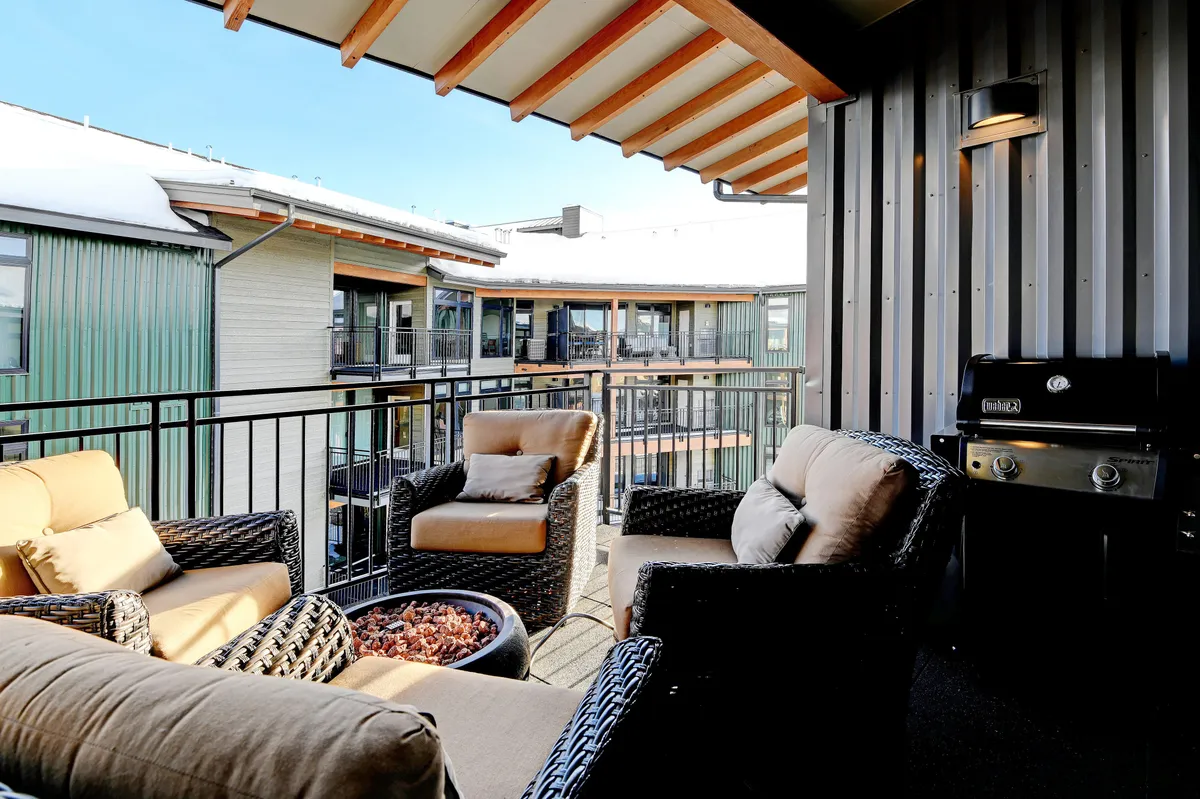 This image features a comfortable outdoor seating area on a balcony, complete with a grill and a decorative fire pit. The view suggests a relaxing spot for enjoying a sunset, dining al fresco, or gathering with friends.