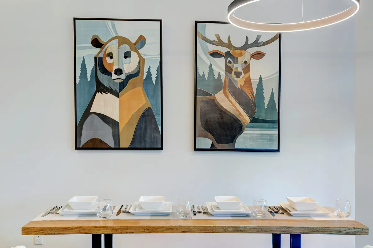 A beautifully set dining table is the focal point, complemented by locally-inspired bear and deer artwork along the walls. The mood is festive and inviting, ideal for shared meals and special celebrations within the open-plan space.