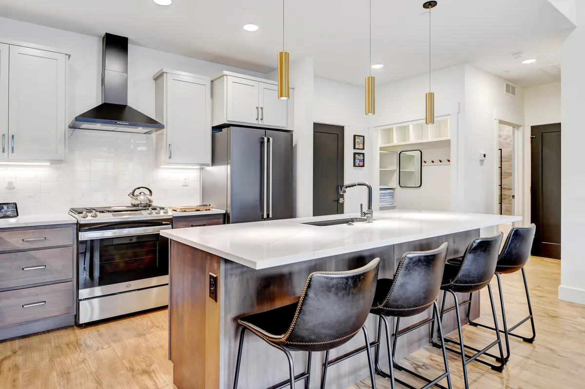 A contemporary kitchen scene with a large island, stainless steel appliances, stylish pendant lighting, and bar stools. The setup is perfect for casual breakfasts, coffee rituals, and engaging conversations while meals are being prepared.