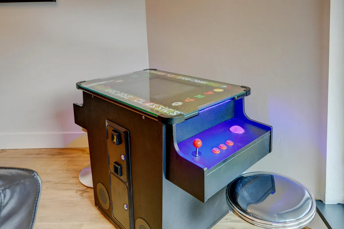 A nostalgic interior scene with an arcade game machine and a stool, inviting guests to play and socialize in a relaxed, friendly space. The focus is on casual enjoyment and shared moments.
