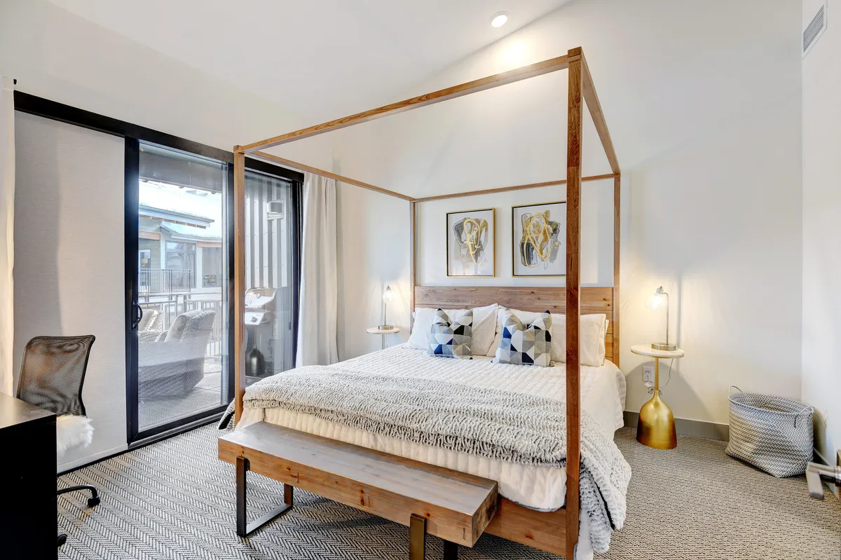 A serene bedroom with a canopy bed, large window offering a mountain or town view, and tasteful framed artwork. Soft natural light fills the room, enhancing the tranquil, restful ambiance.