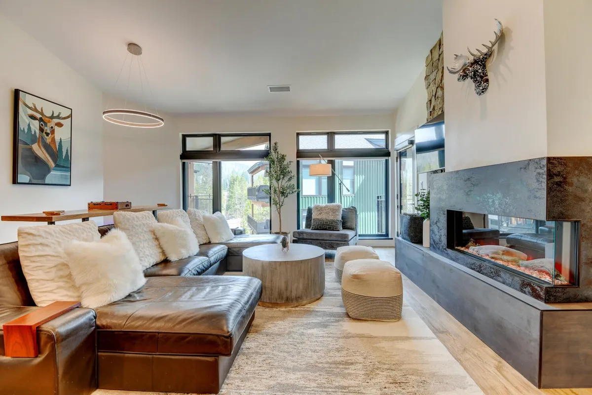 The image showcases a stylish, modern living room with a plush sofa, a circular coffee table, a glowing fireplace, and tasteful artwork on the wall. The space exudes warmth and comfort, inviting guests to gather, relax, and enjoy cozy evenings indoors.